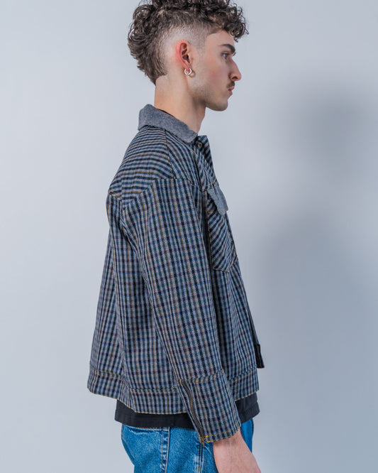 Man wearing a wool plaid jacket and jeans against a plain background. The jacket is sustainable and unisex, made from upcycled high quality wool materials.