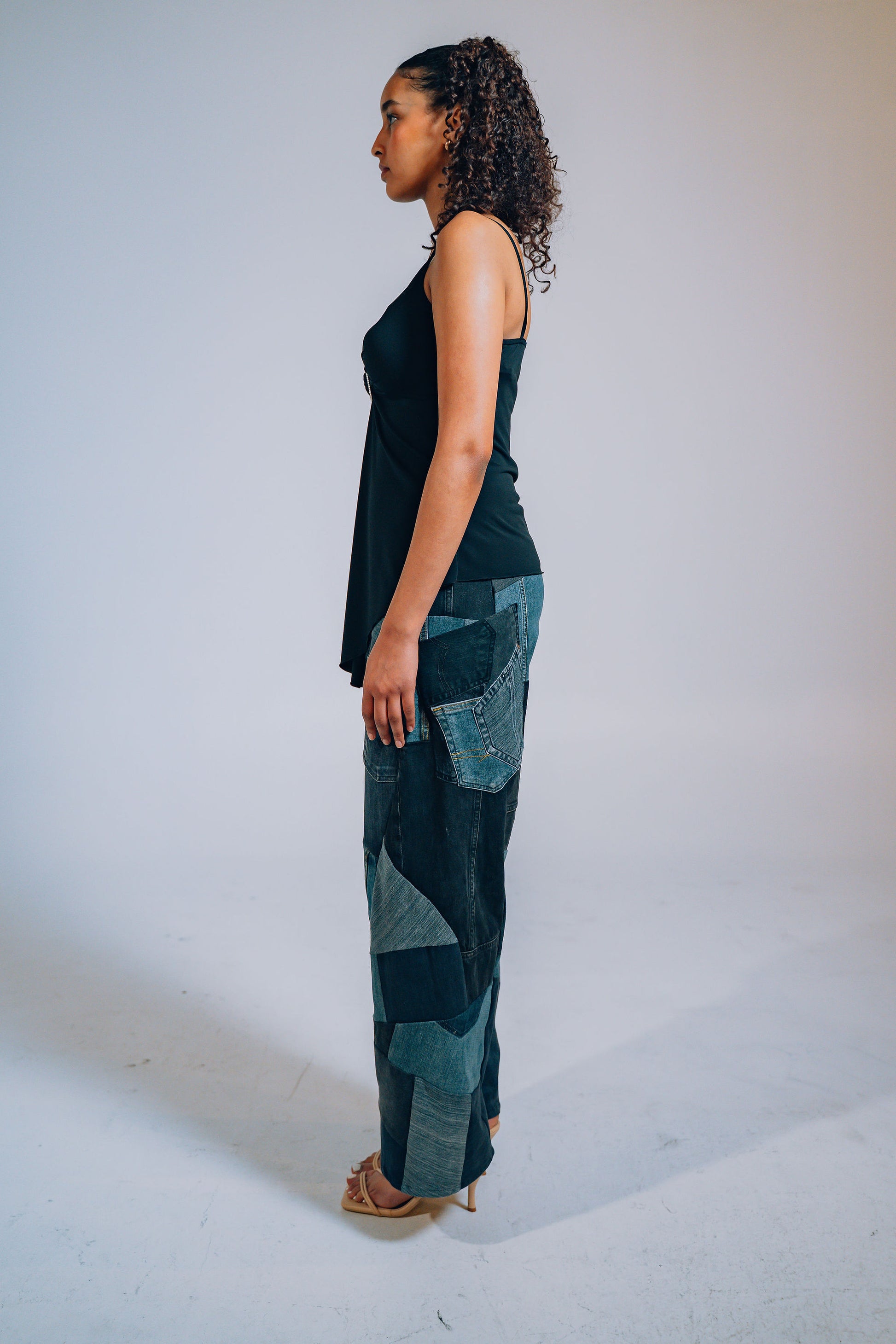 Woman wearing a black sleeveless top and patchwork pants against a white background