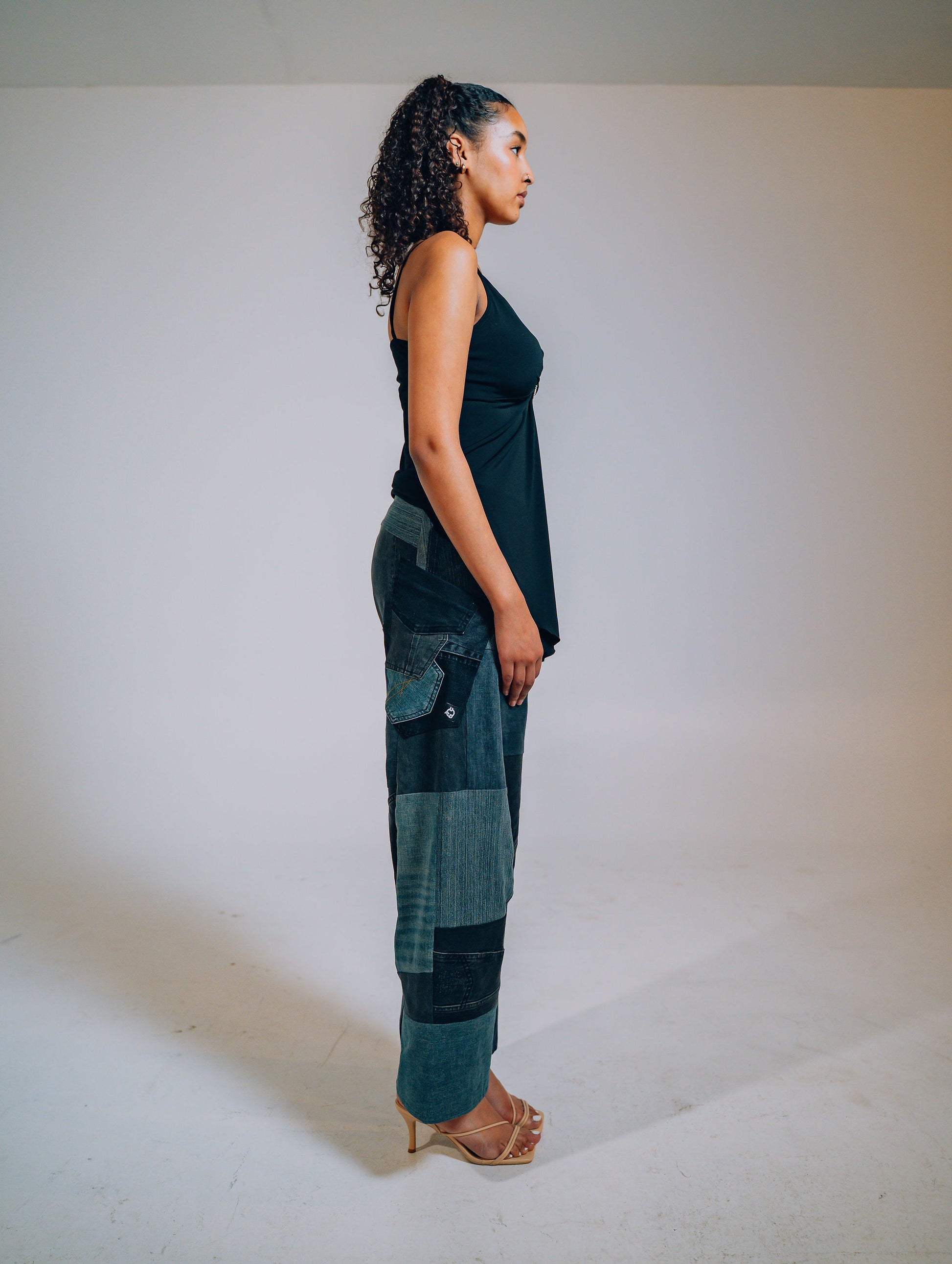 Woman wearing a black sleeveless top and patchwork pants against a white background