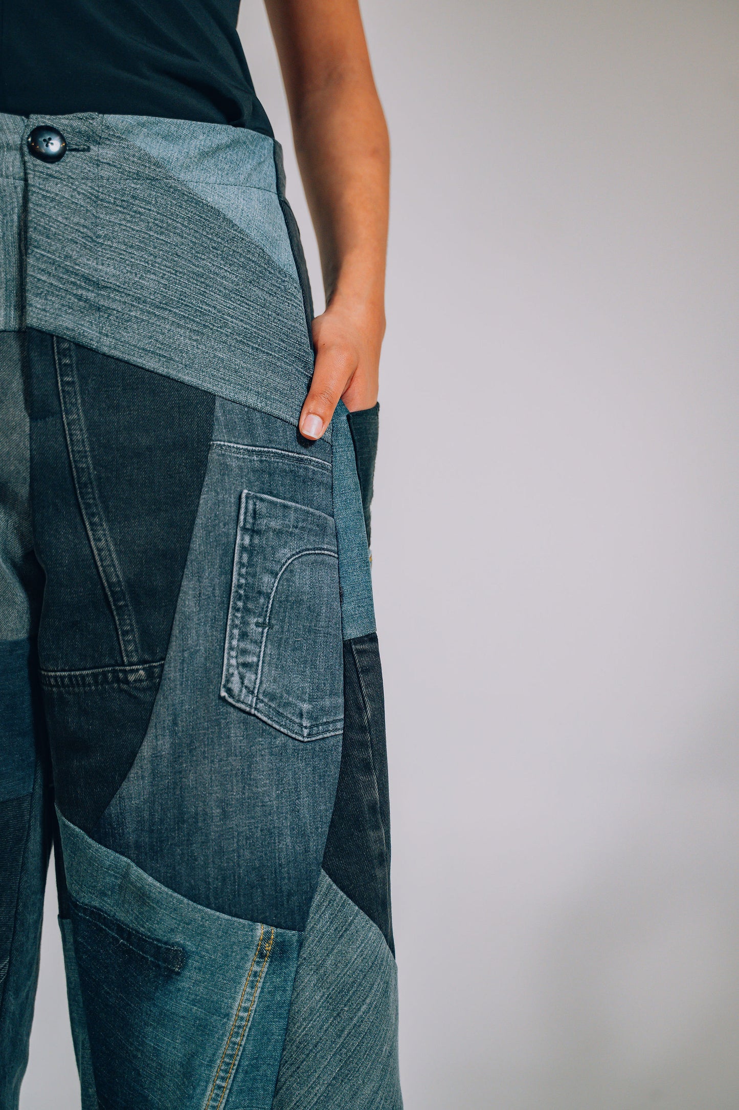 Close-up of a person wearing patchwork jeans against a plain background