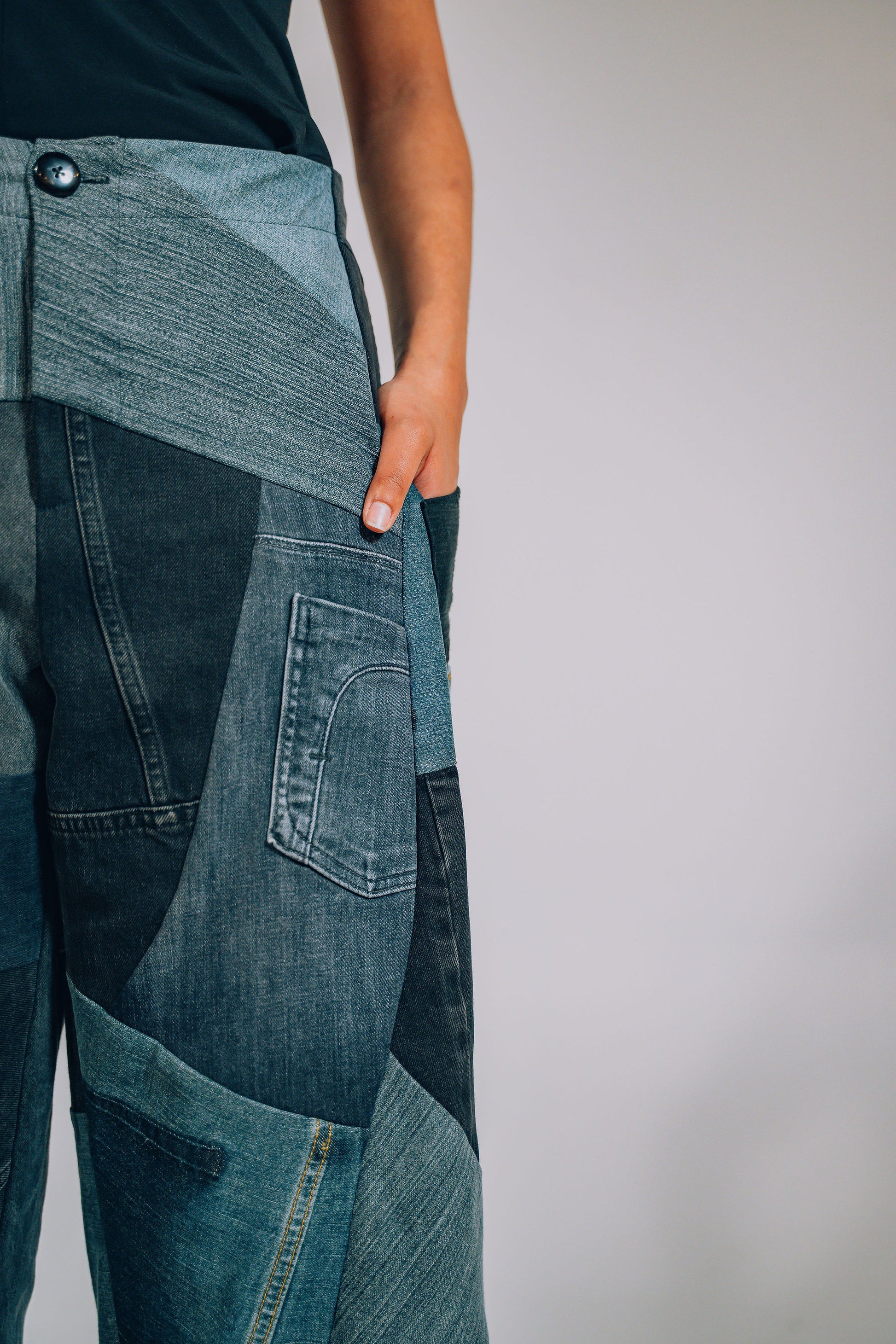 Close-up of a person wearing patchwork jeans against a plain background