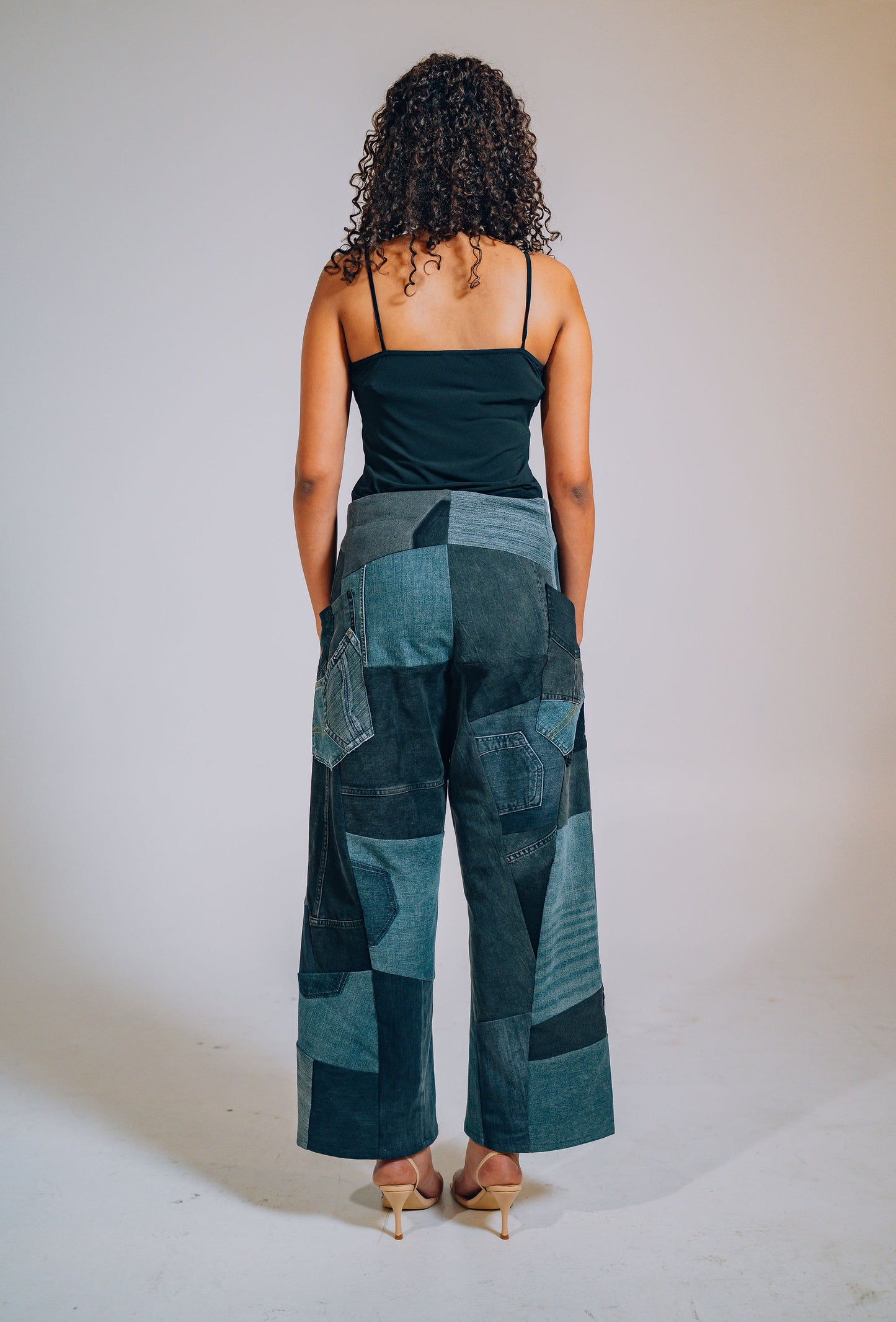 Woman wearing a black top and patchwork pants against a plain background