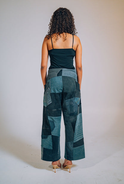 Woman wearing a black top and patchwork pants against a plain background