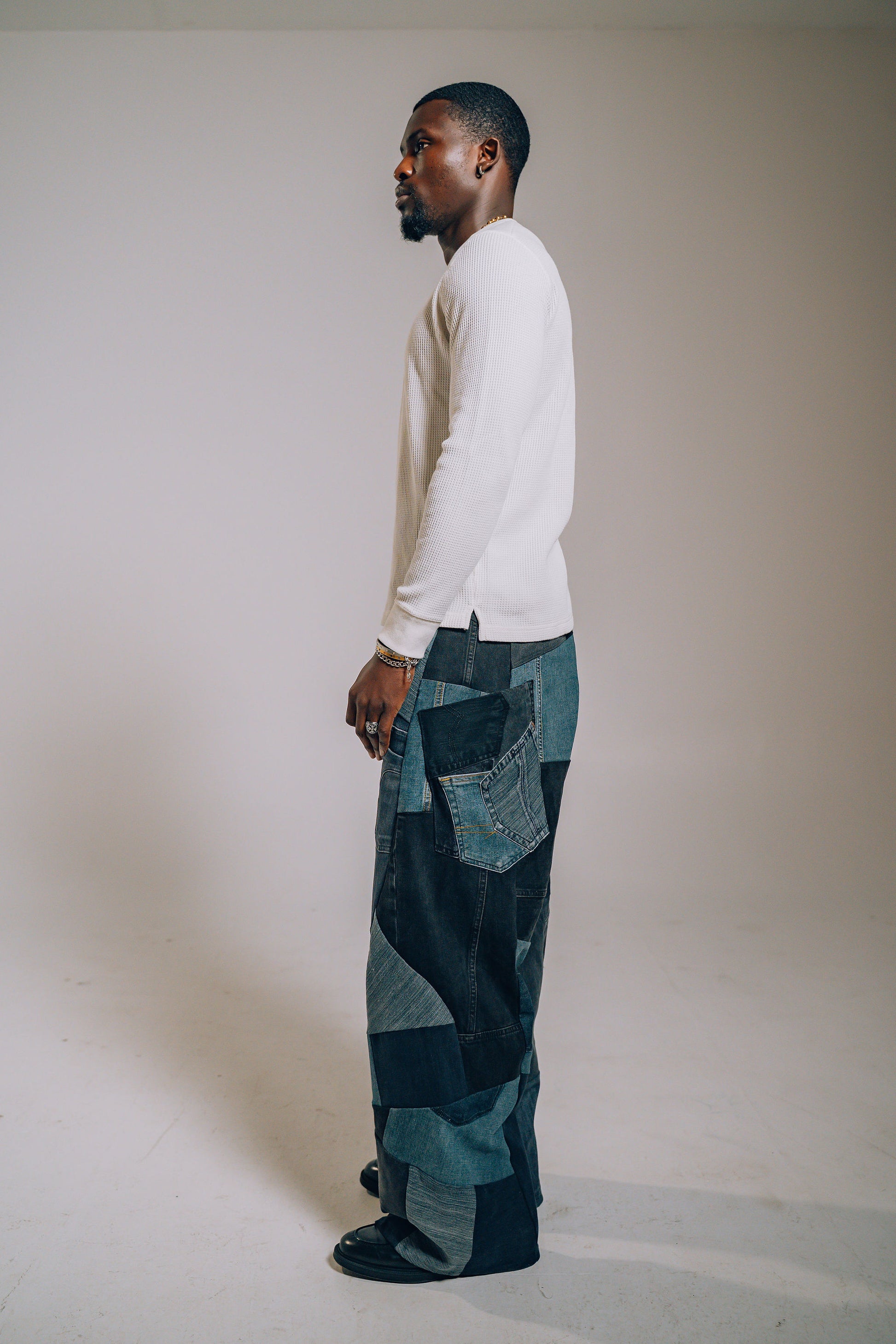 Man wearing a white long-sleeve shirt and patchwork pants against a plain background