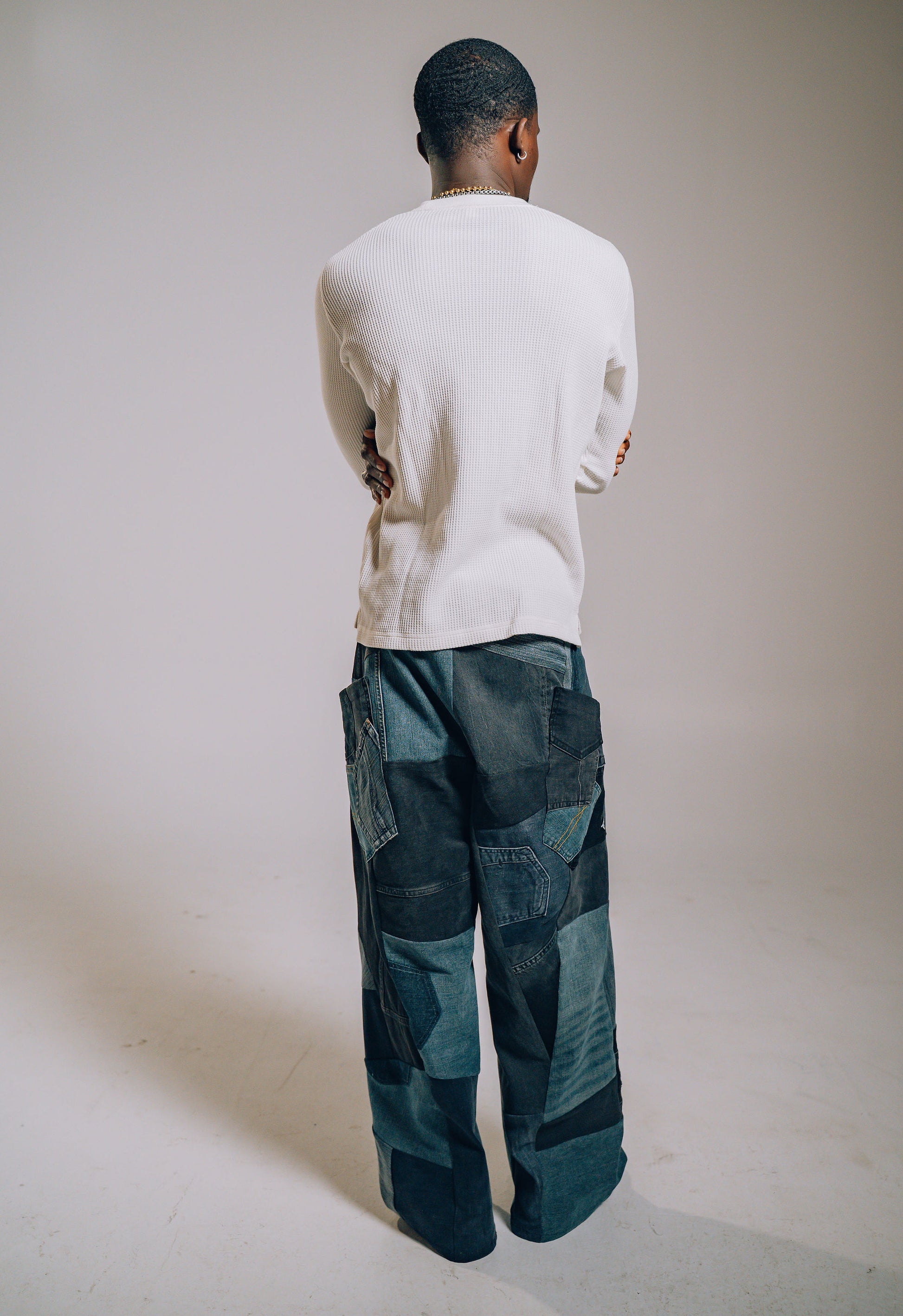 Person wearing a white sweater and patchwork pants against a plain background
