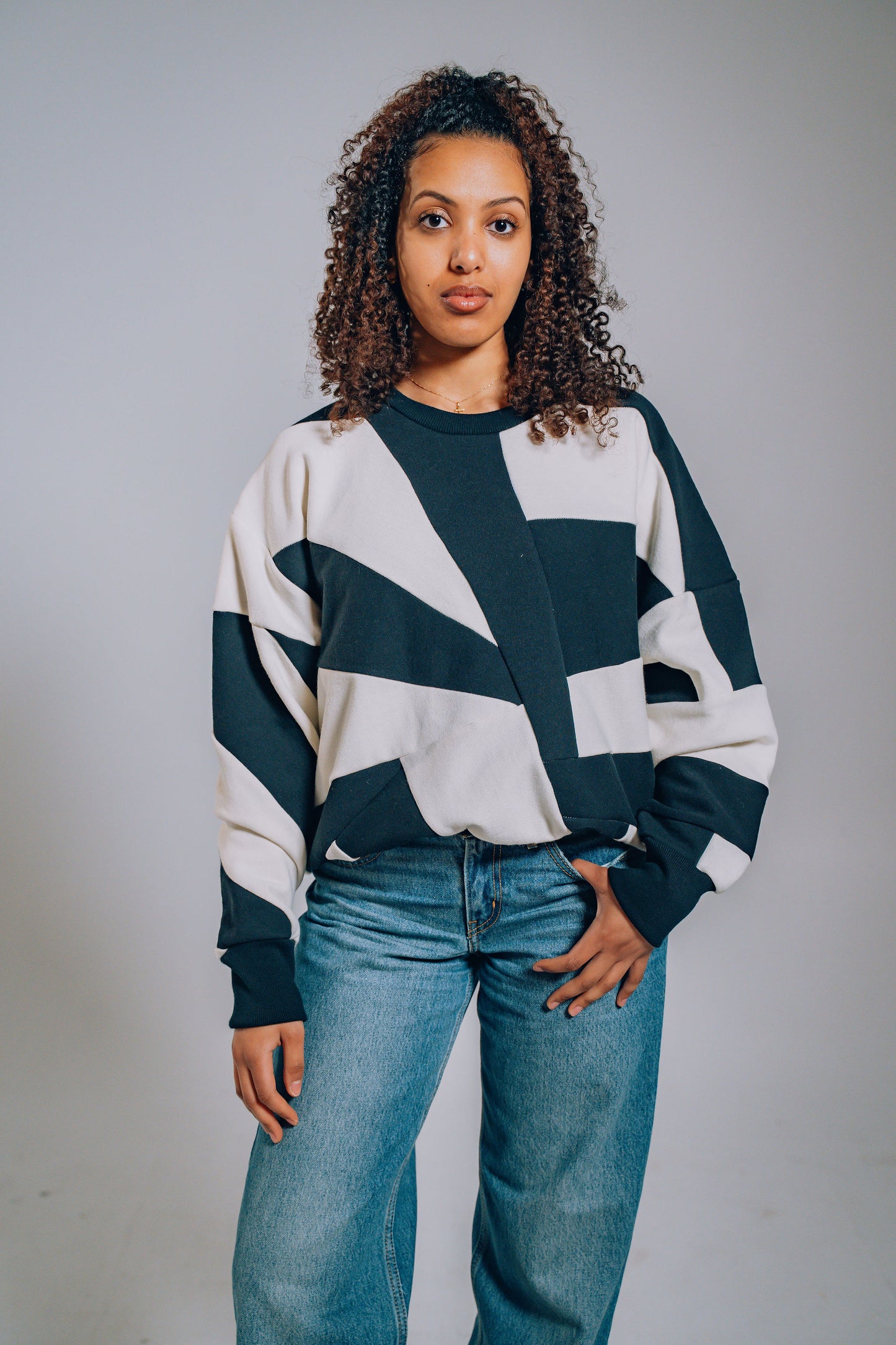 Woman wearing a black and white geometric sweater with blue jeans against a gray background
