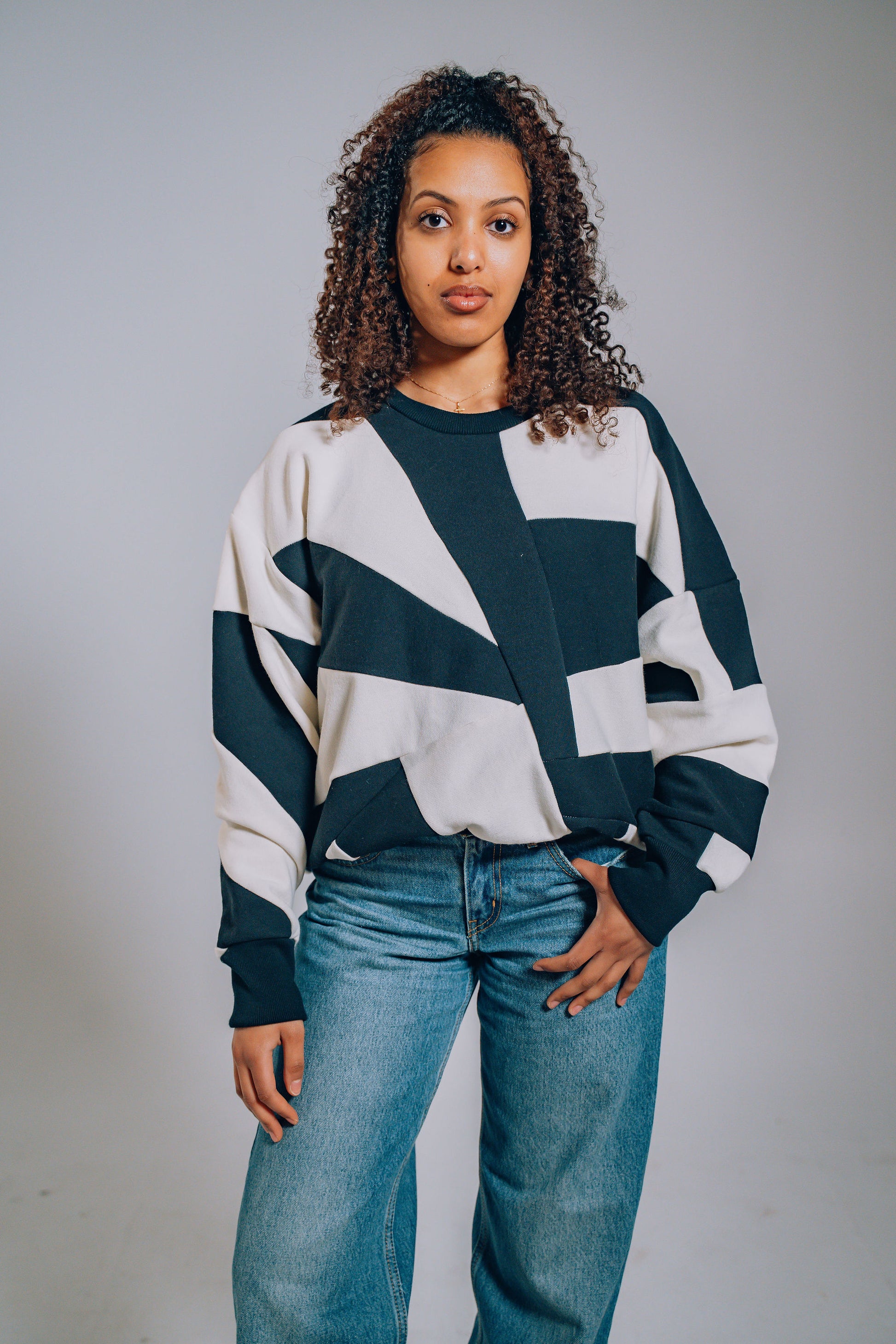 Woman wearing a black and white geometric sweater with blue jeans against a gray background