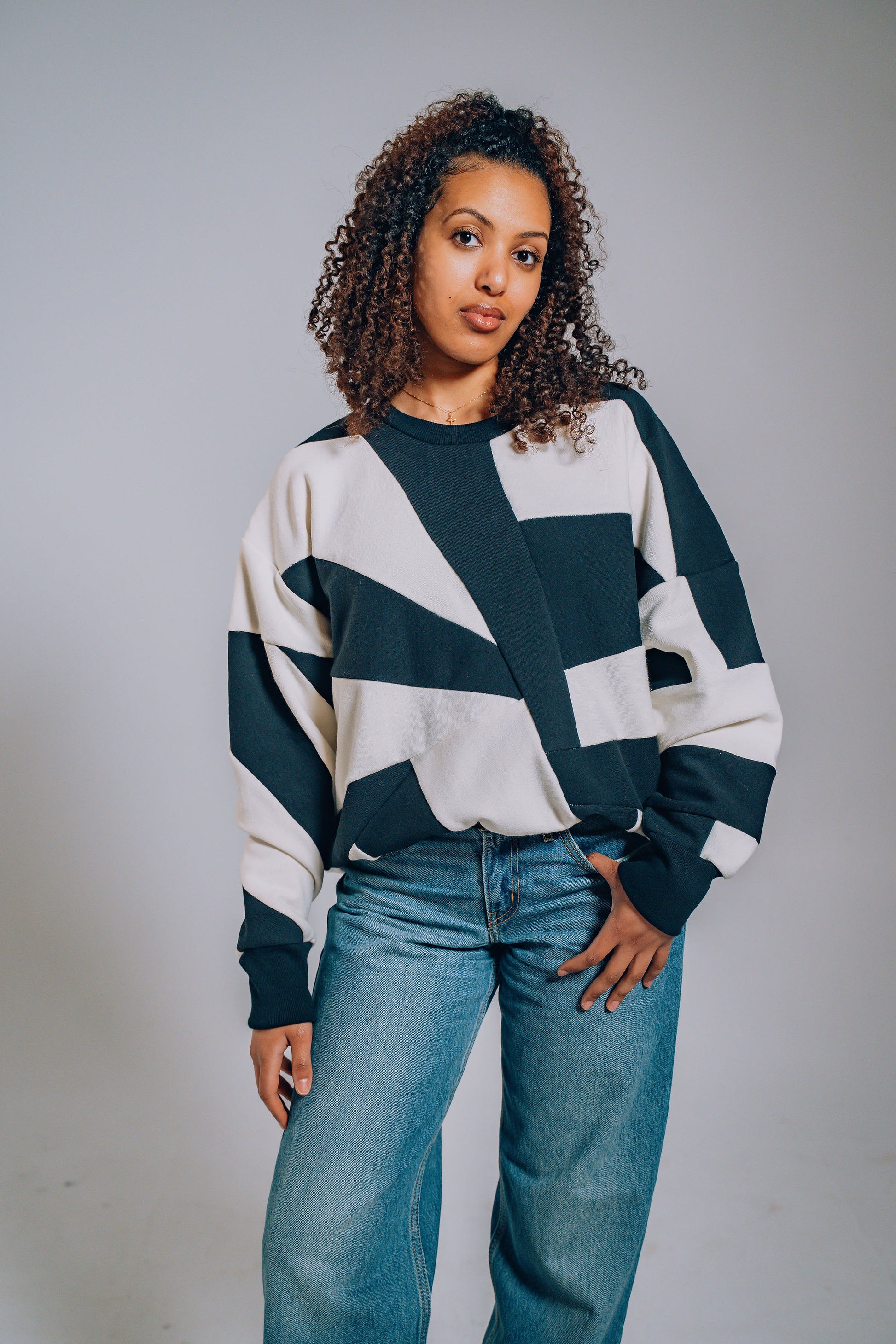 Woman wearing a black and white patterned sweater with blue jeans against a plain background