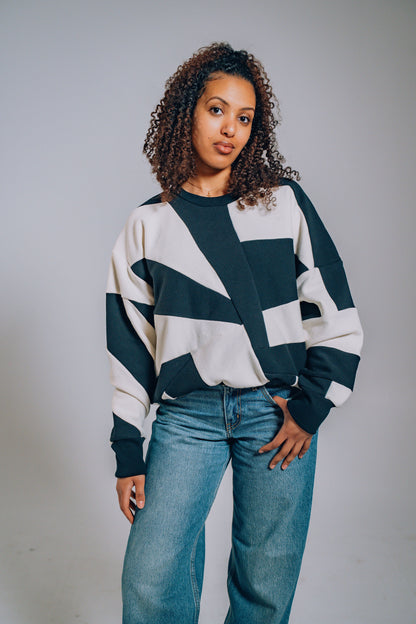 Woman wearing a black and white patterned sweater with blue jeans against a plain background