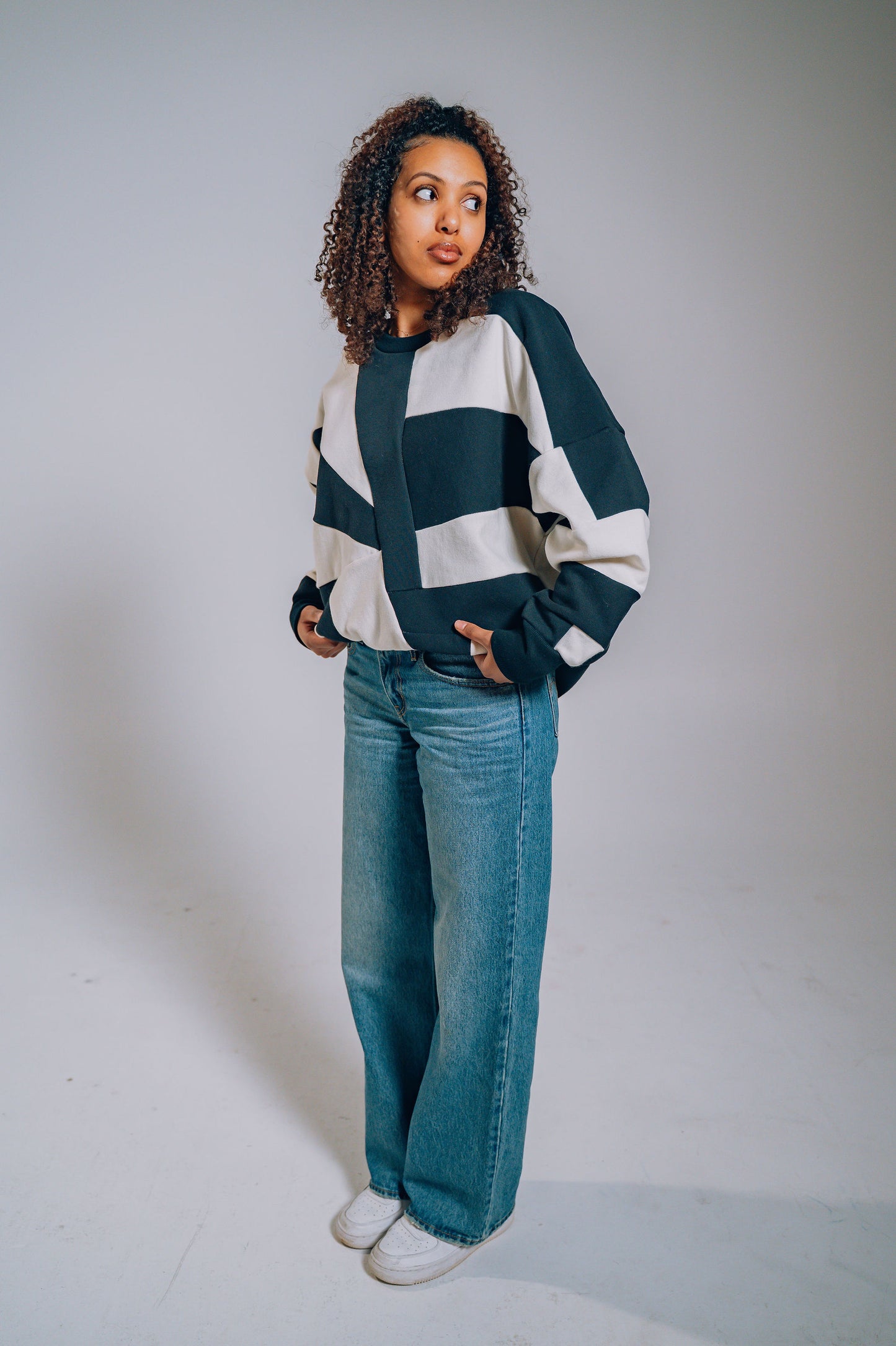 Person wearing a black and white patchwork sweater and jeans against a plain background