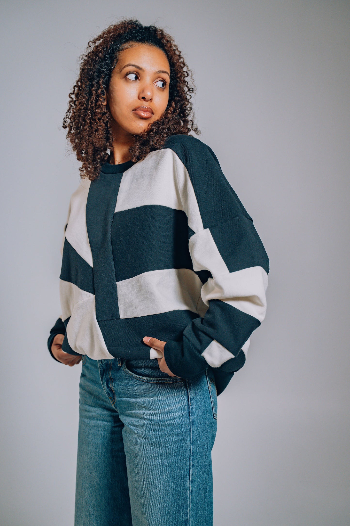 Woman wearing a black and white patchwork sweater with blue jeans against a plain background