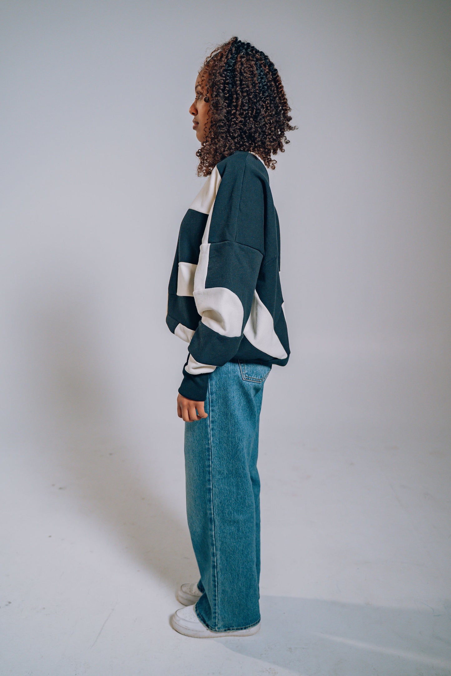 Person wearing a black and white patchwork sweater and blue jeans on a plain background