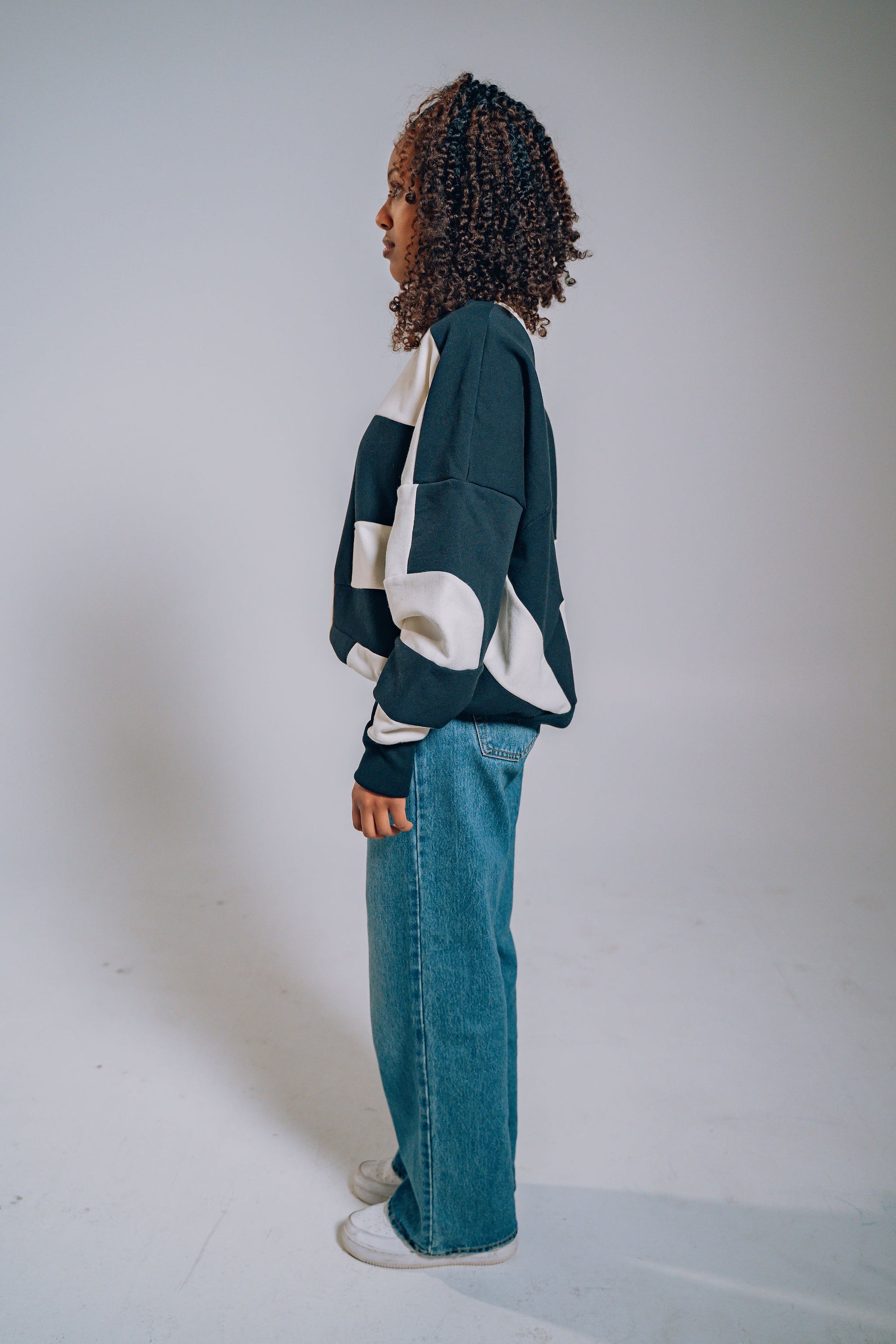 Person wearing a black and white patchwork sweater and blue jeans on a plain background