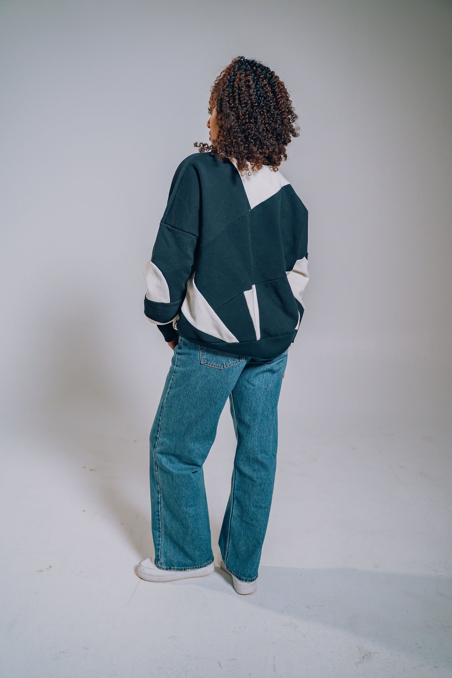 Person wearing a black and white patchwork sweater and blue jeans on a plain background