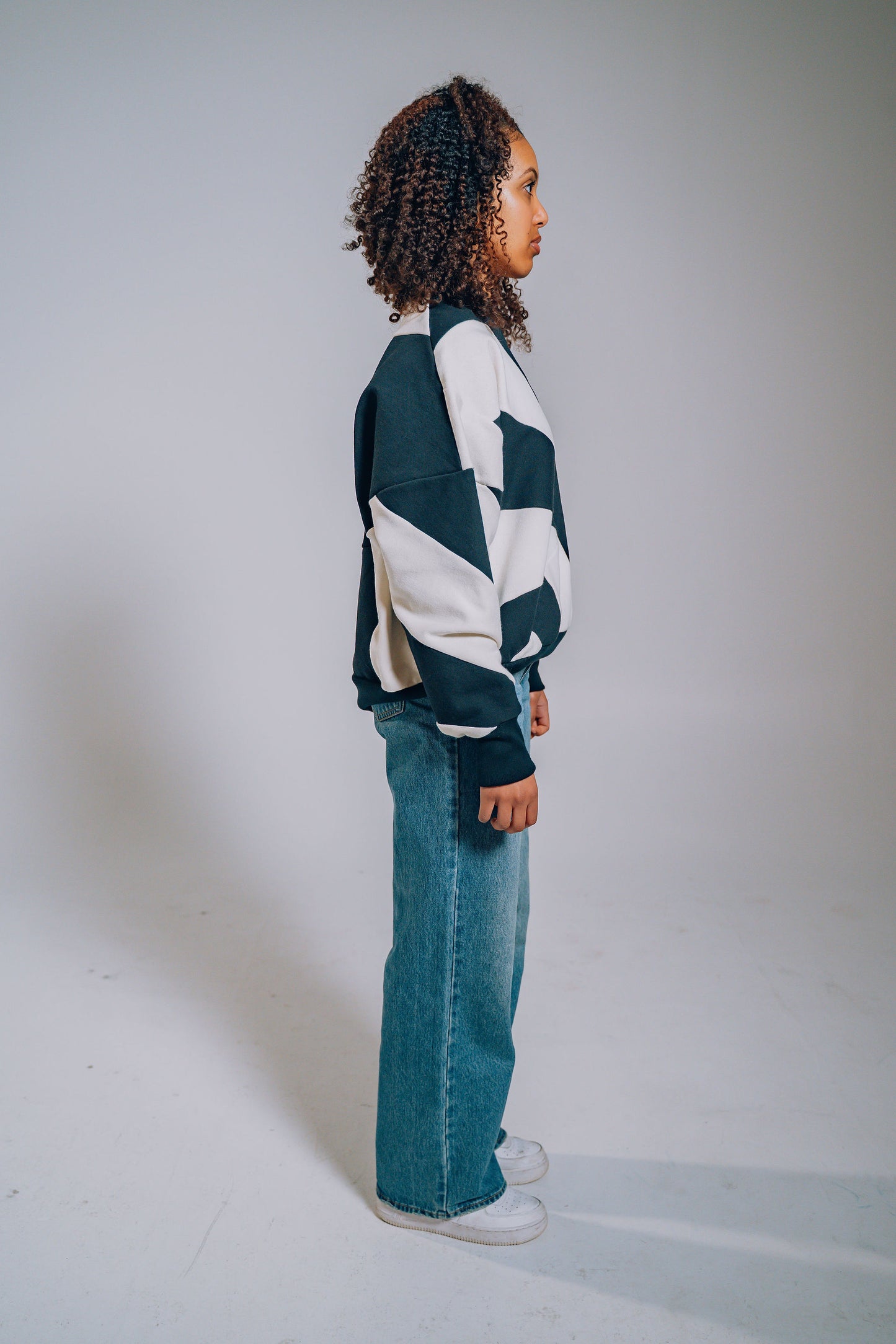 Person wearing a black and white patchwork sweater and blue jeans on a plain background