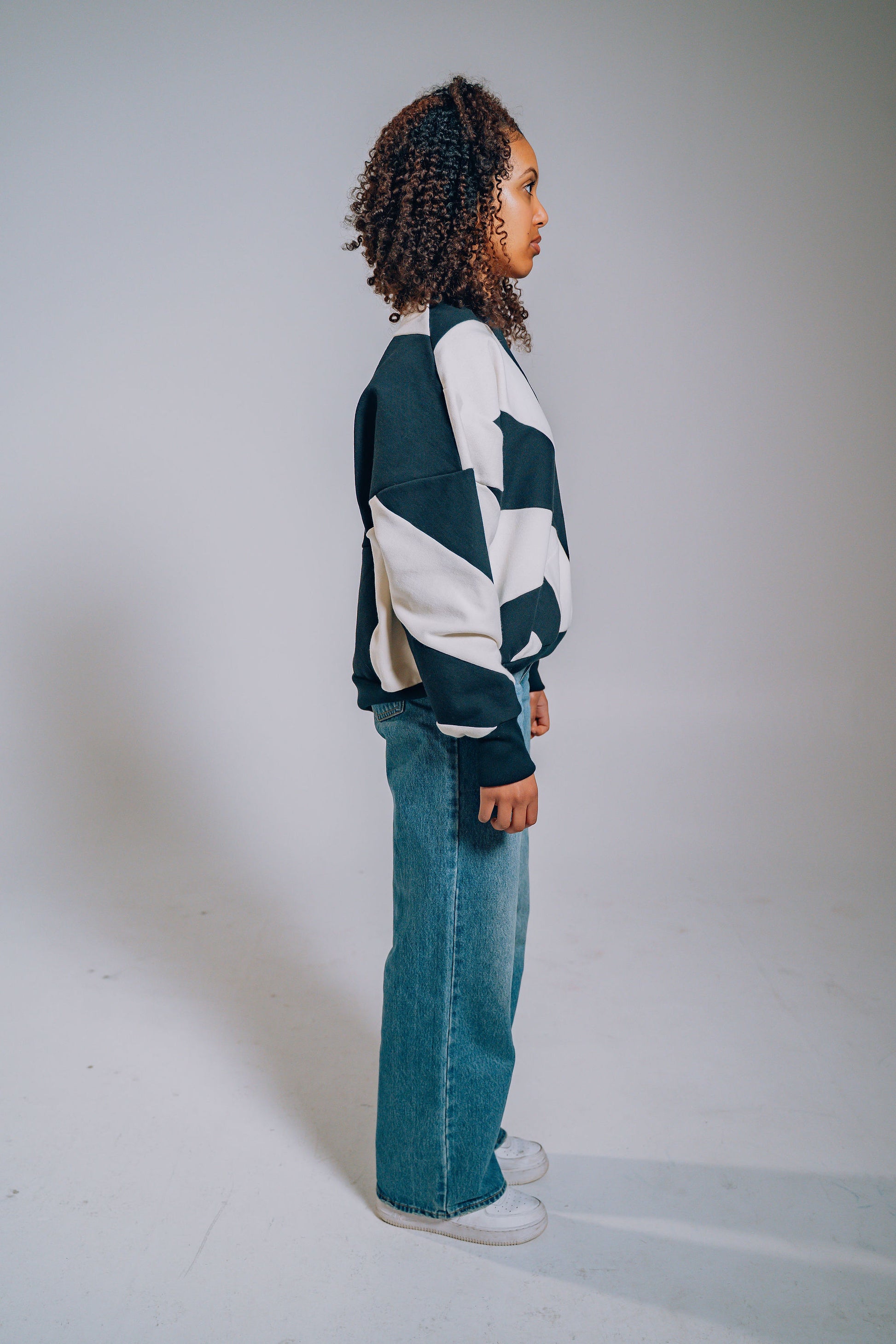 Person wearing a black and white patchwork sweater and blue jeans on a plain background