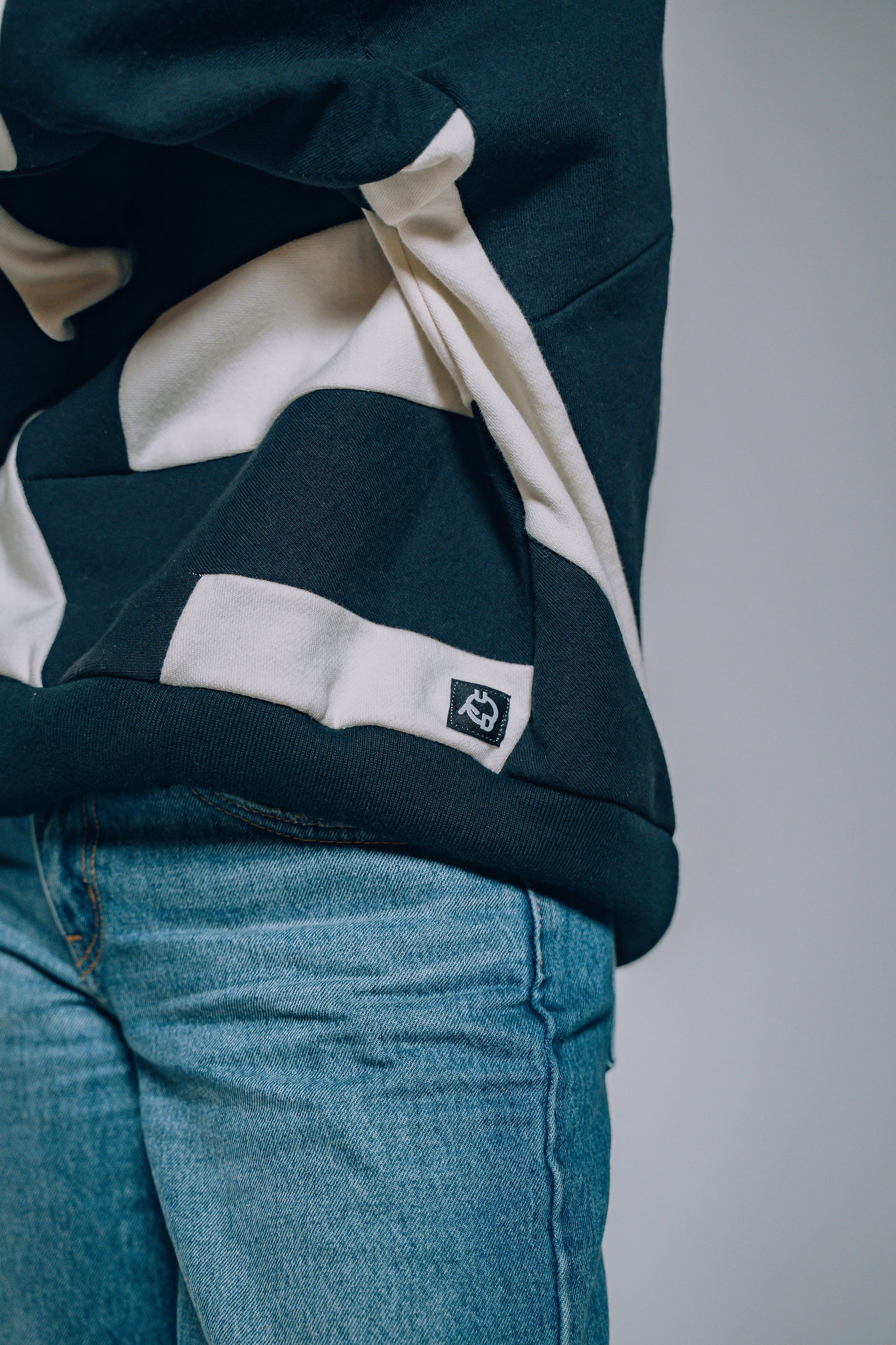 Person wearing a black and white patchwork sweater and blue jeans on a plain background