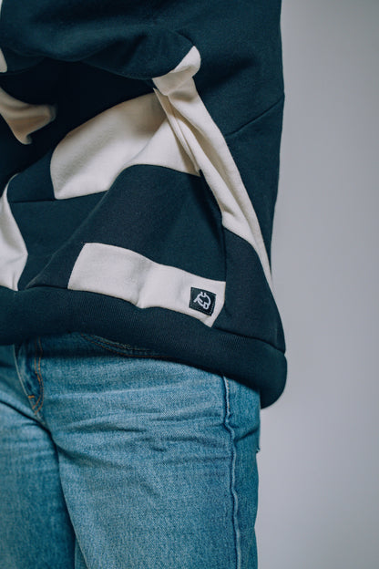 Person wearing a black and white patchwork sweater and blue jeans on a plain background