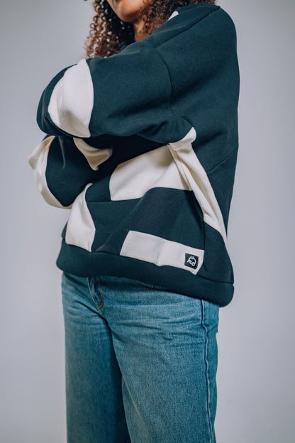 Person wearing a black and white patchwork sweater and blue jeans on a plain background
