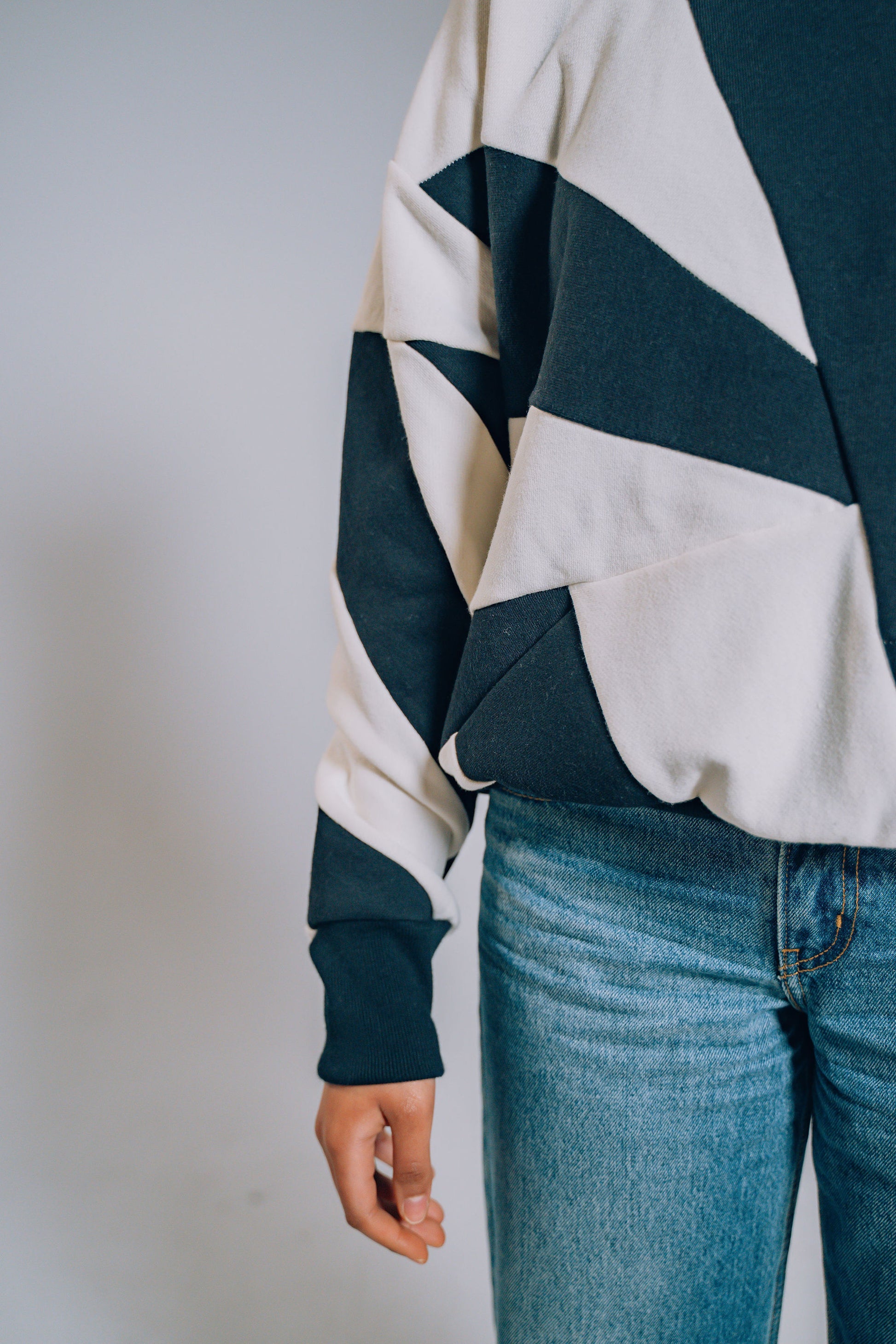 Person wearing a black and white patchwork sweater and blue jeans on a plain background