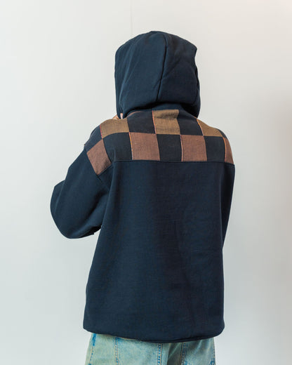 The back of a person wearing a black and brown checkered hoodie against a white background. Hoodie is made from upcycled materials and is sustainable and unisex.
