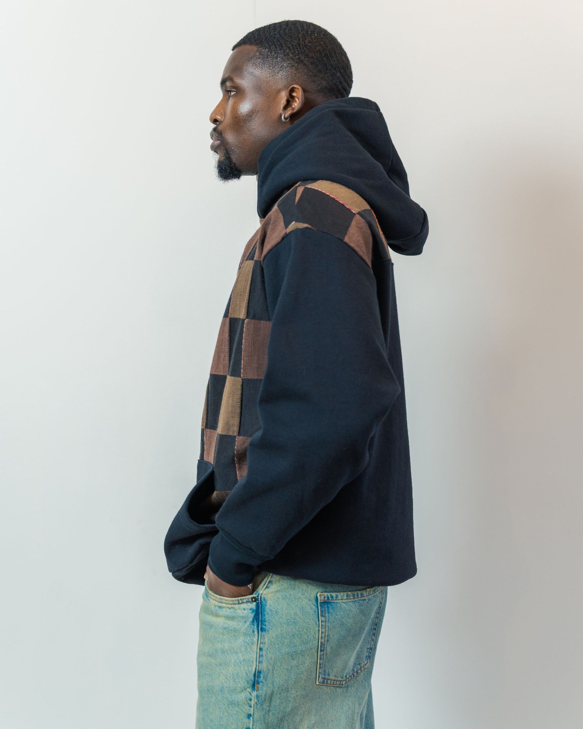 Man wearing a black hoodie with a checkered pattern on a plain background. Hoodie is made from sustainable upcycled textiles.