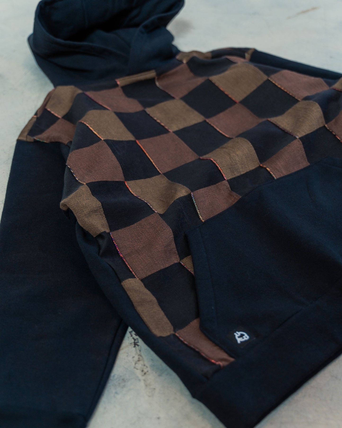 Hoodie on the ground showing stitchwork details and black and brown checkered fabric.