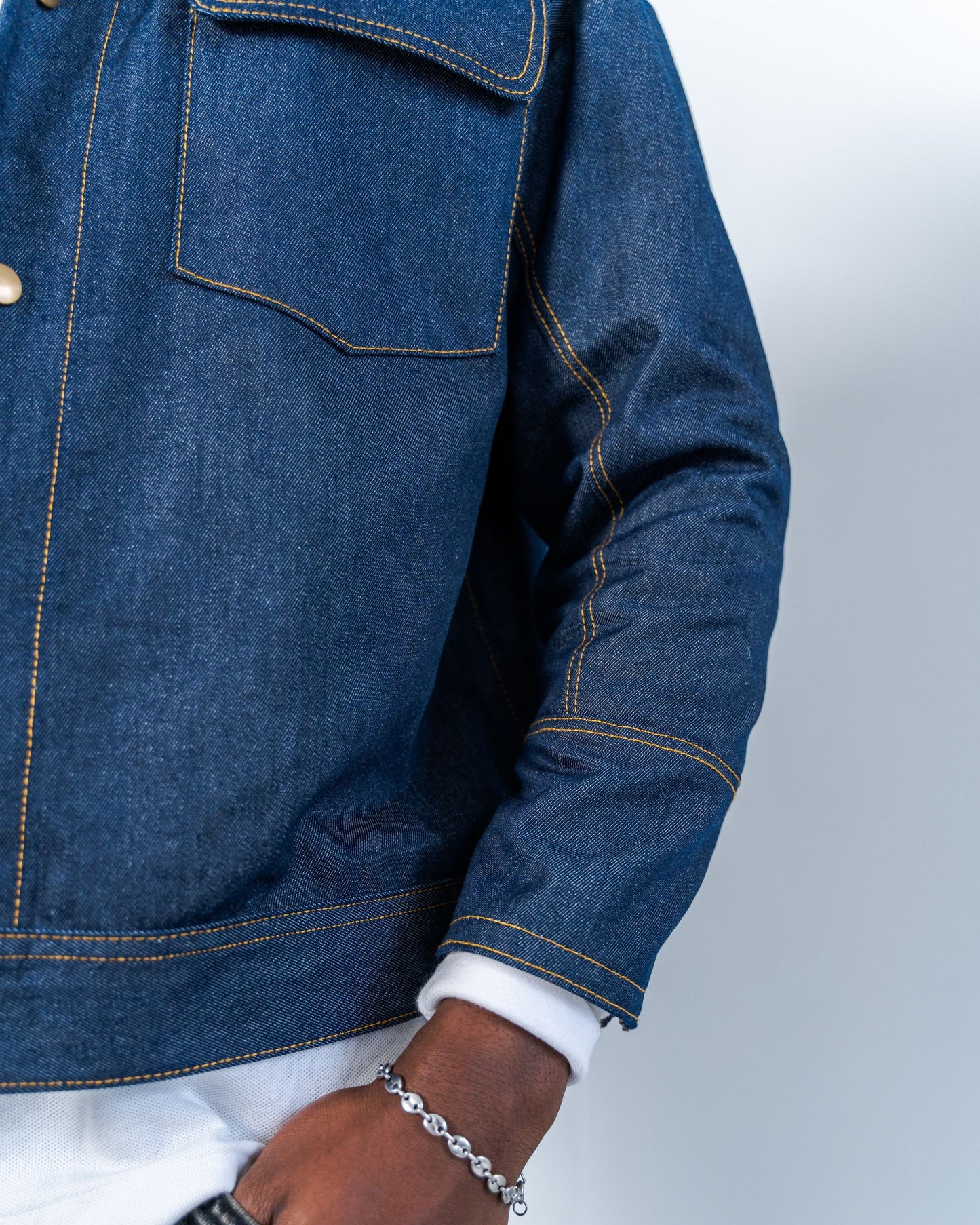 Close-up of a person wearing a blue raw denim jacket on a white background