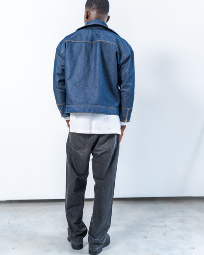Person wearing a blue denim jacket and gray pants against a white background