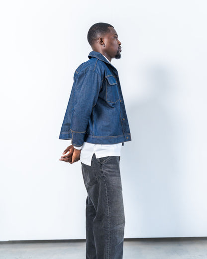 Man wearing a blue raw denim jacket and gray pants against a white background
