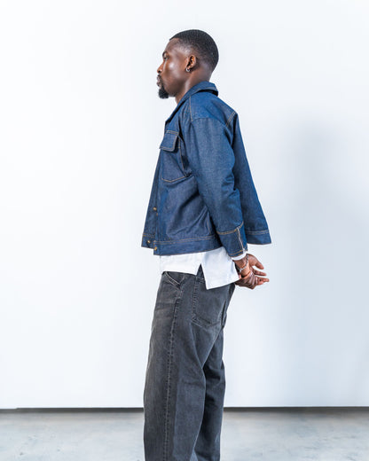 Man wearing a blue raw denim jacket and dark jeans against a white background
