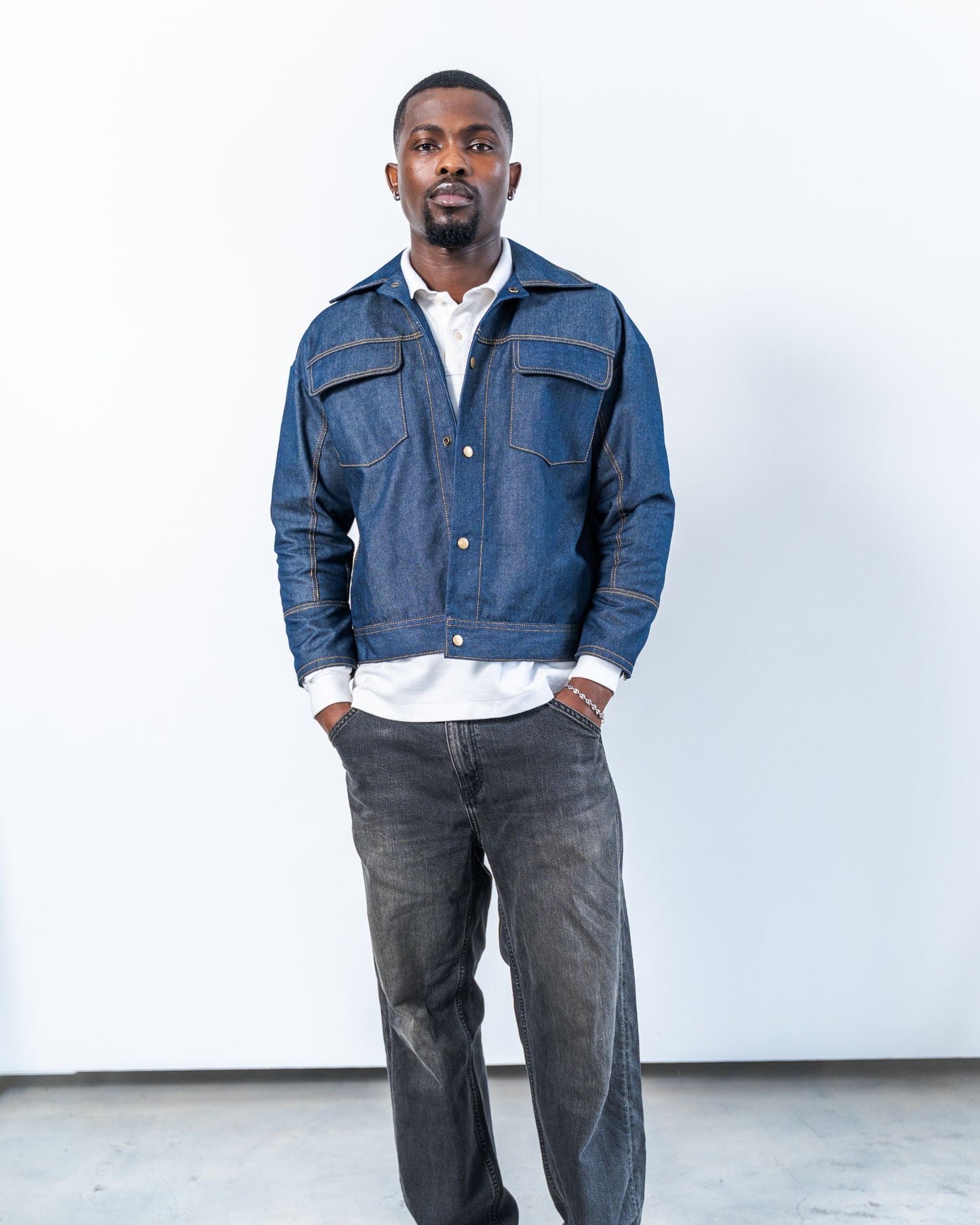 Man wearing a blue raw denim jacket and dark jeans against a white background